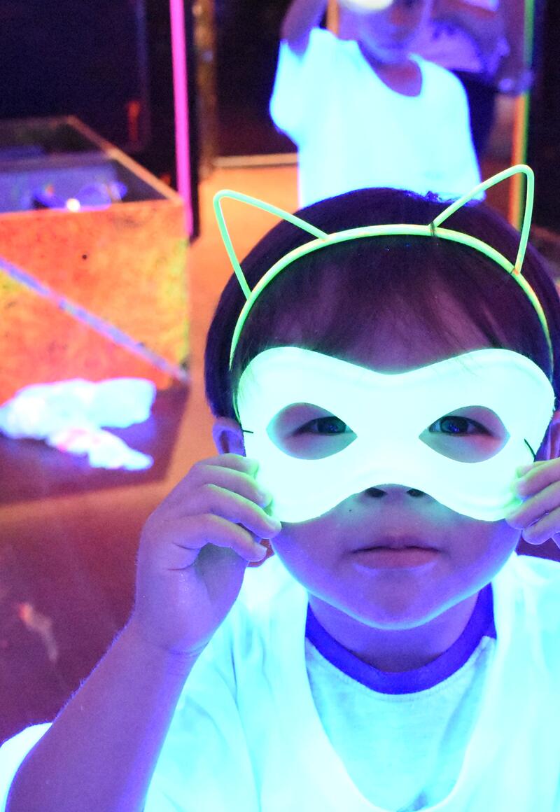 Child holding a glowing neon cat mask at a Sketch Studios blacklight party